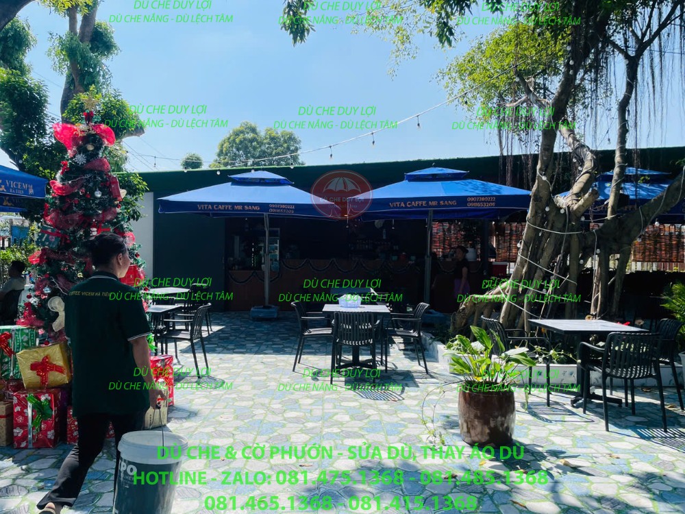 Dù lệch tâm vuông màu xanh che khu bàn ghế ngoài trời trước quán cafe.